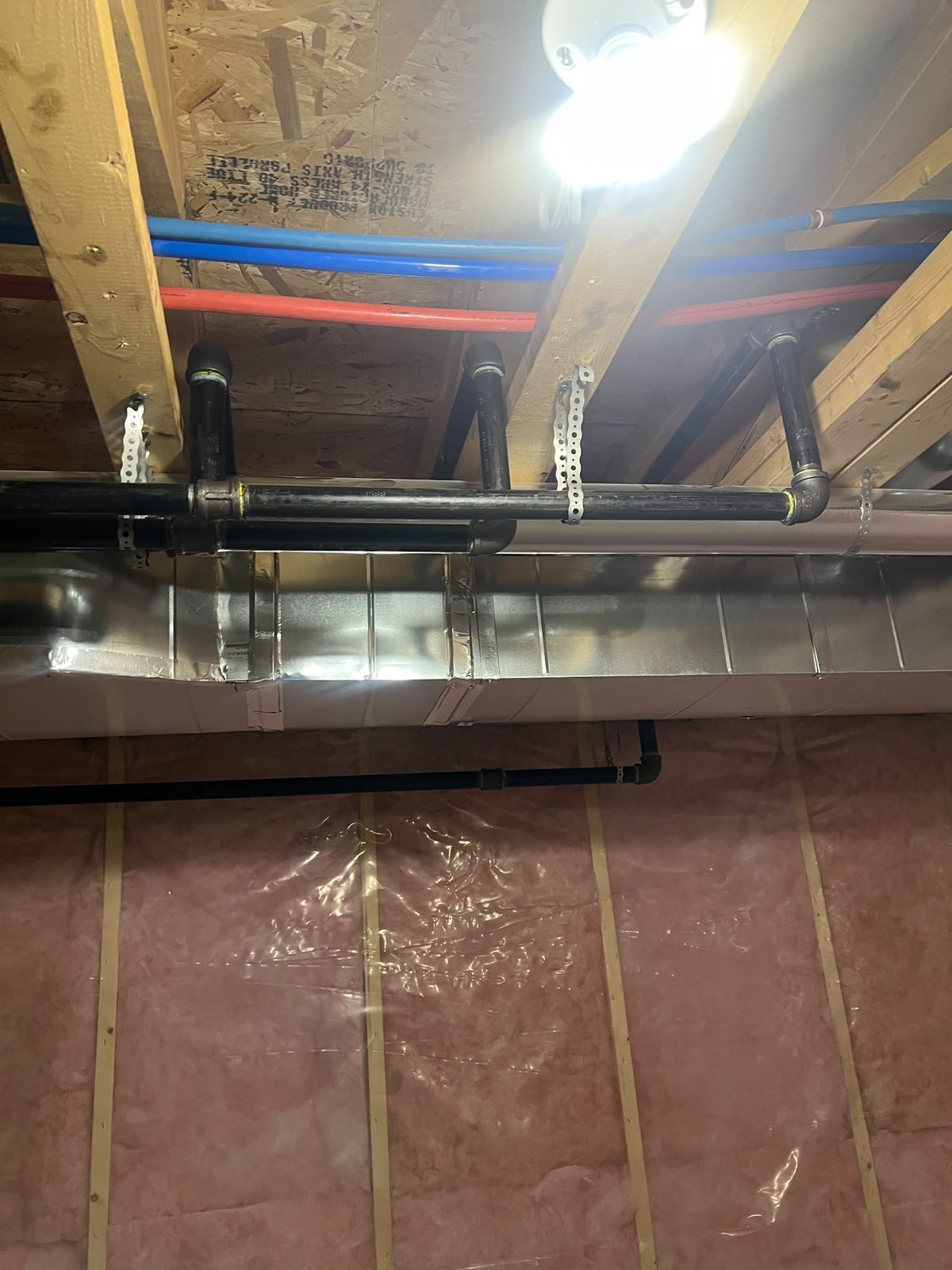 Black iron gas line rough-in secured along basement floor joists