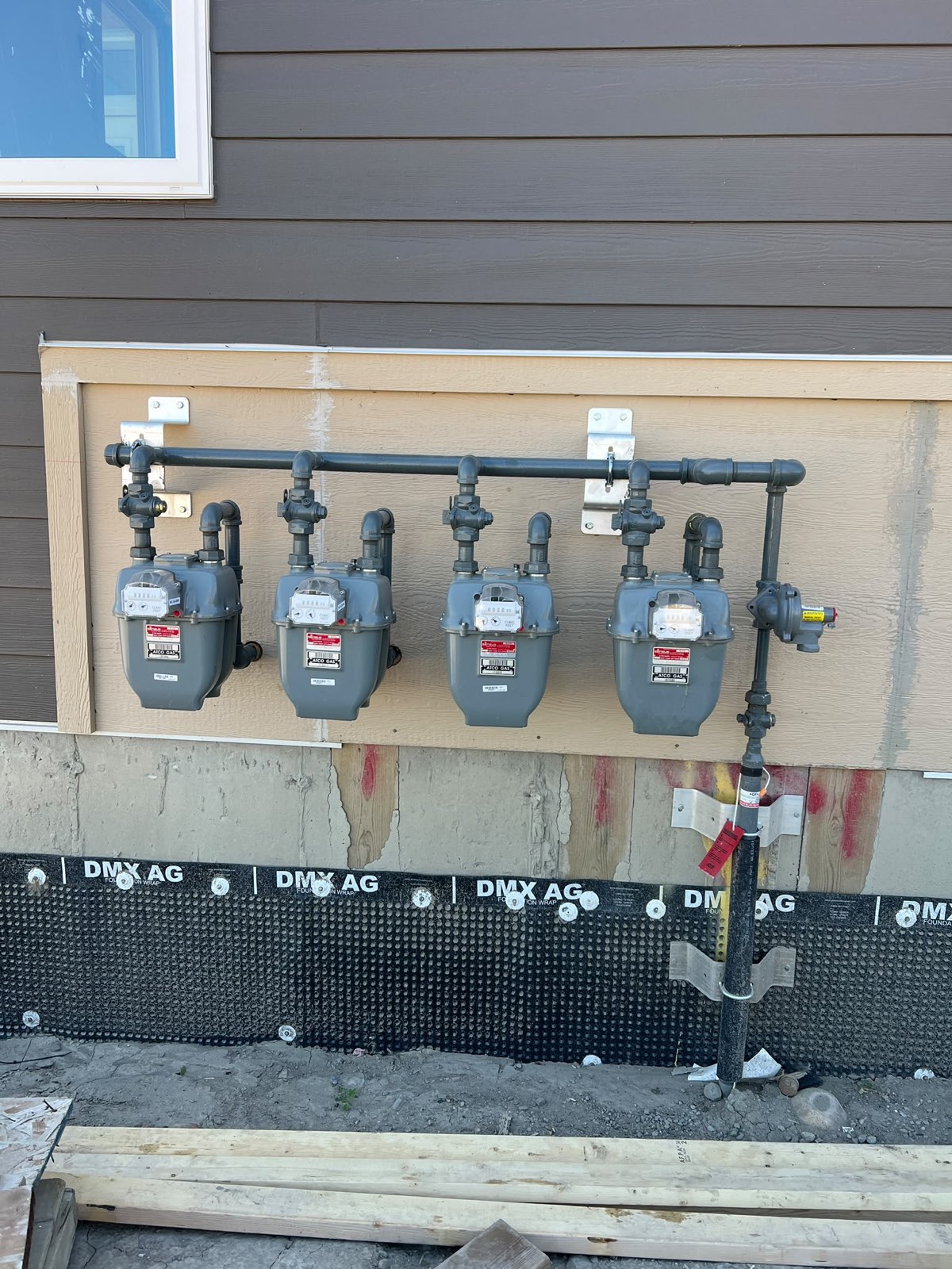 Bank of four natural gas meters piped and mounted on a multi-unit building